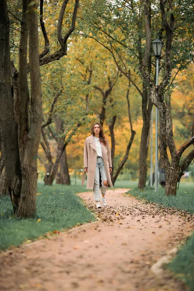 Europejska Dziewczyna Różowym Płaszczu Niebieskich Dżinsach Otworami Spaceruje Jesiennym Parku — Zdjęcie stockowe