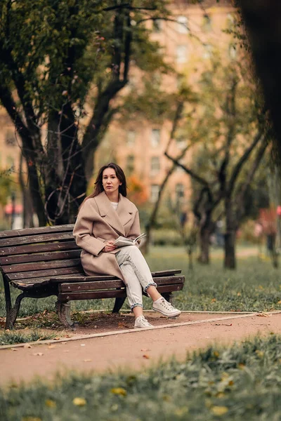 Uma Menina Caucasiana Com Casaco Bege Jeans Azul Senta Banco — Fotografia de Stock