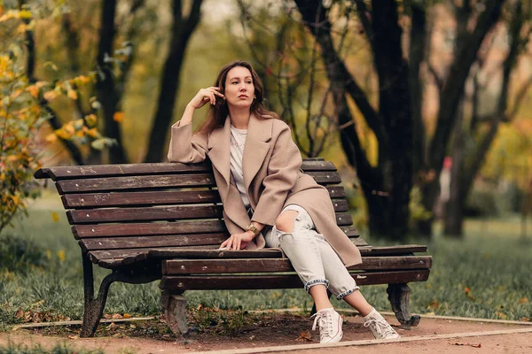 Una Chica Caucásica Con Abrigo Beige Vaqueros Azules Sienta Banco — Foto de Stock