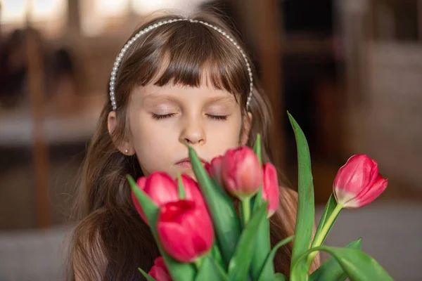 A six-year-old girl in a pink dress holds red tulips in her hands