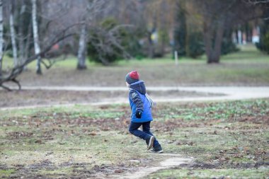 Altı yaşında, mavi elbiseli bir beyaz çocuk parkta yürüyor.