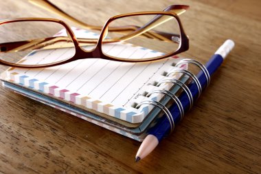 Renkli küçük spiral defter, gözlük ve ahşap bir masa üzerinde bir kalem