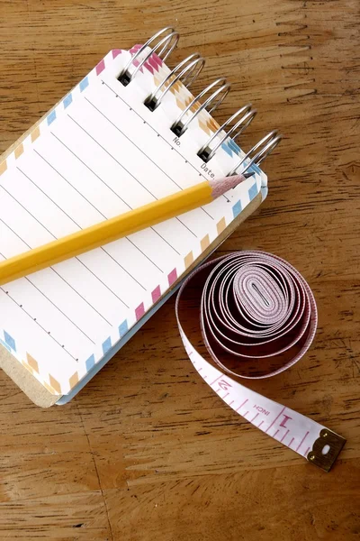 Barevné malé spirály zápisník, tužku a Svinovací metr na dřevěný stůl — Stock fotografie