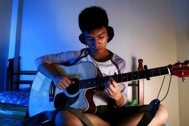 Genç çocuk bir yatakta bir gitar ile oynarken