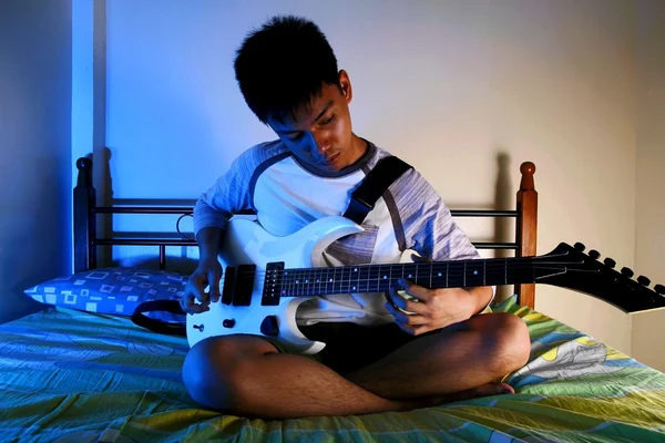 Tonårspojke leker med en gitarr på en säng — Stockfoto