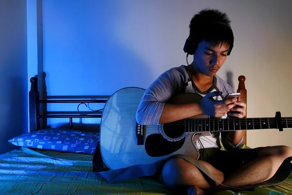 Tonårspojke leker med en gitarr på en säng — Stockfoto
