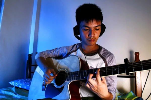 Teenage boy playing with a guitar on a bed — Stock Photo, Image