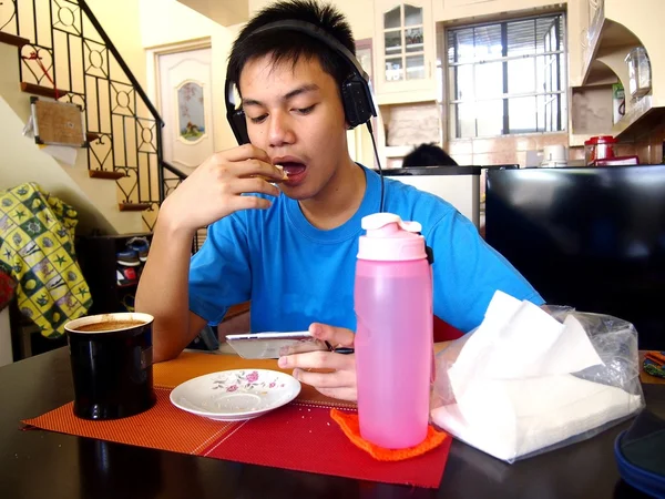 Jovem adolescente fazendo um lanche enquanto assiste em um dispositivo móvel — Fotografia de Stock