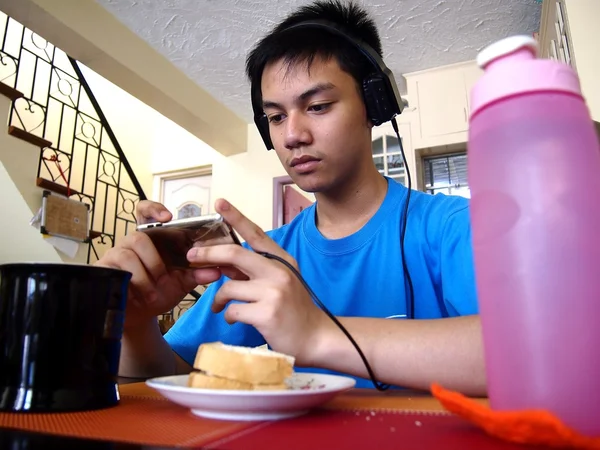 Adolescente joven tomando un aperitivo mientras ve en un dispositivo móvil — Foto de Stock