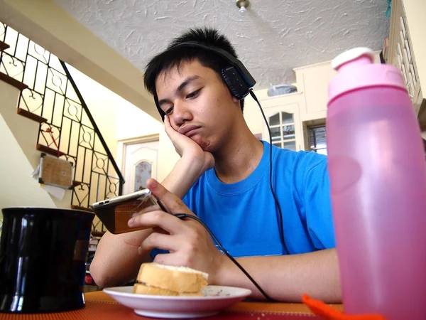 Adolescente joven tomando un aperitivo mientras ve en un dispositivo móvil —  Fotos de Stock