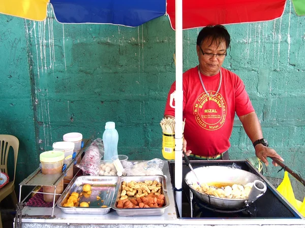 Un vendedor de alimentos cocina bolas de pescado, salchichas y huevos de codorniz que vende en un carrito de comida — Foto de Stock