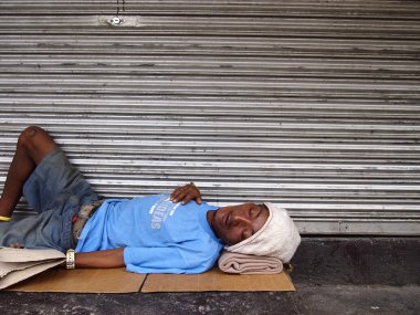 Bir adam kapalı bir dükkanın hemen dışındaki kaldırımda uyuyor.