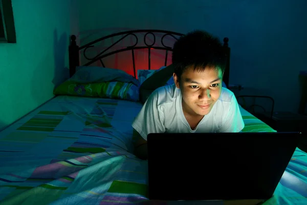 Junger Teenager vor einem Laptop und auf einem Bett — Stockfoto