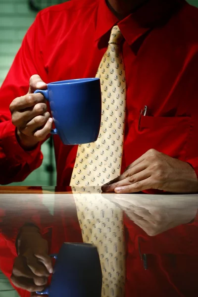 男は赤の長袖シャツ、黄色のネクタイを着ていると、コーヒーのマグカップを保持 — ストック写真