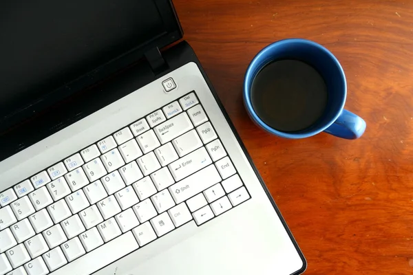便携式计算机和一个蓝色的咖啡杯在桌子上 — 图库照片