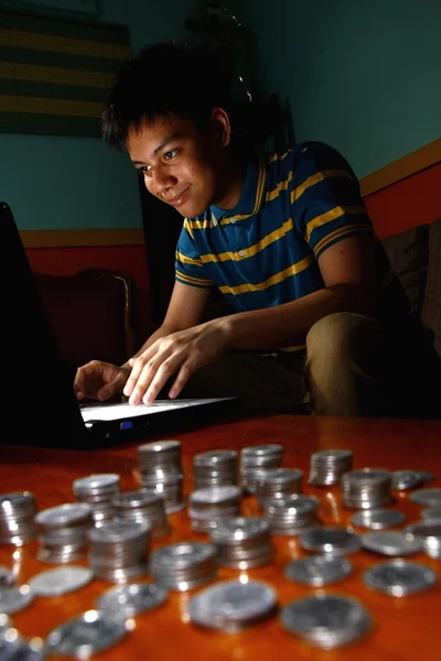 Asiática adolescente en frente de ordenador portátil y una pila de monedas — Foto de Stock