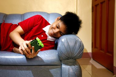 Teen kanepede uzanmış ve gülümseyen bir smartphone kullanarak