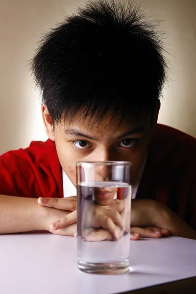 Adolescente guardando un bicchiere d'acqua su un tavolo di legno — Foto Stock