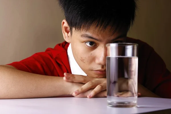 Adolescente olhando para um copo de água em uma mesa de madeira — Fotografia de Stock