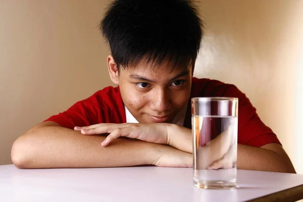 Teen looking at a glass of water on a wooden table — Stock Photo, Image