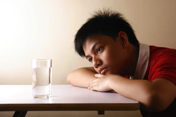 Teenager blickt auf ein Glas Wasser auf einem Holztisch — Stockfoto