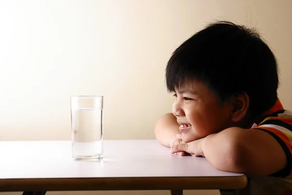 Niño mirando un vaso de agua en una mesa de madera — Foto de Stock