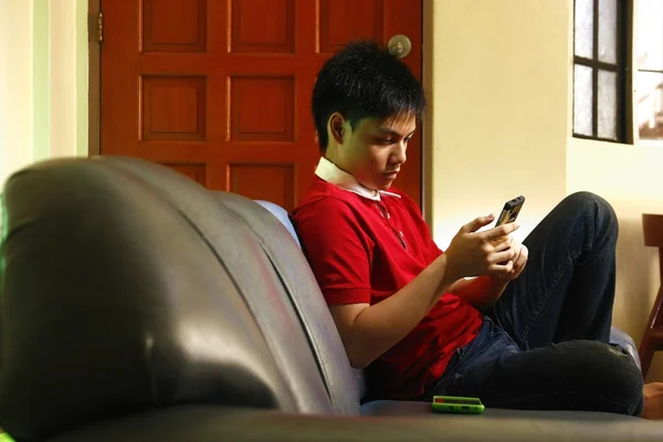 Teen using a smartphone while sitting on couch — Stock Photo, Image