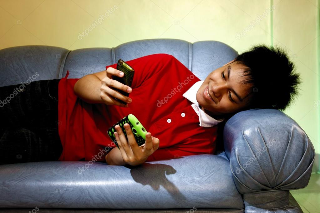 Sad Young Female Student Sitting On Bed, Using Smartphone 