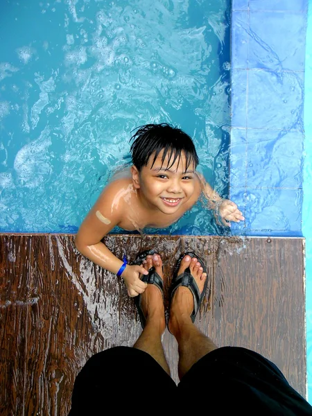 Young boy in a swimming pool and the feet of his parent — Stock Photo, Image