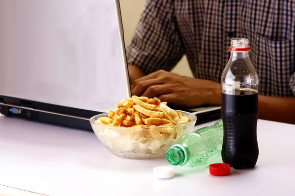 Botellas de refrescos o refrescos, patatas fritas y el hombre que trabaja en una computadora portátil en el fondo — Foto de Stock