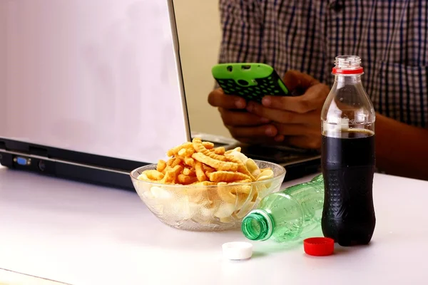 Botellas de refrescos o refrescos, patatas fritas y el hombre que trabaja en una computadora portátil en el fondo — Foto de Stock