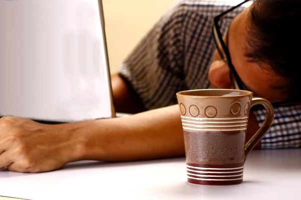 Taza de café y hombre durmiendo en frente de una computadora portátil en el fondo —  Fotos de Stock