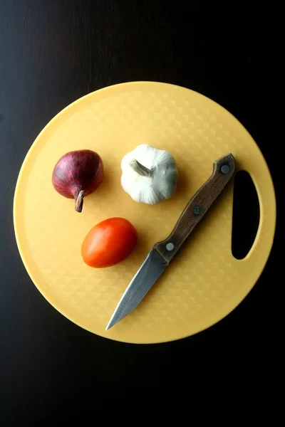 Cebola, alho, tomate e faca na tábua de cortar — Fotografia de Stock