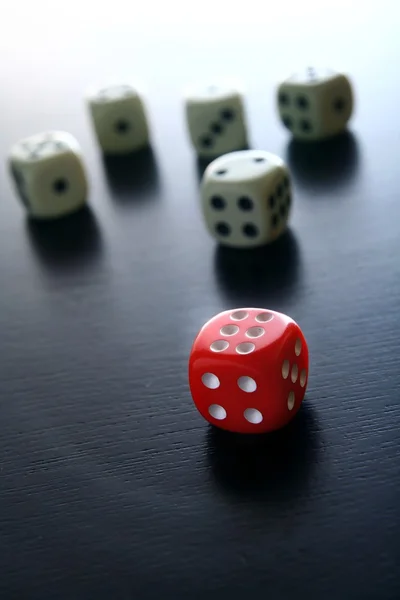 Ein roter Spielwürfel vor fünf weißen Spielwürfeln — Stockfoto