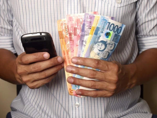 Man håller i en smartphone och filippinska peso räkningar — Stockfoto