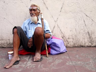 An old man sits on a sidewalk in Antipolo city