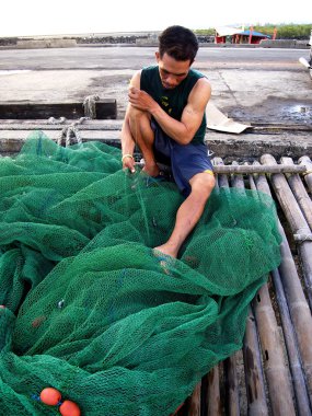 A fisherman repairs a fishing net before casting it out into the sea again.