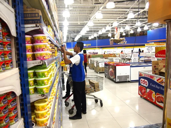 Pracovník uspořádá potravinářských výrobků na polici v obchodě — Stock fotografie