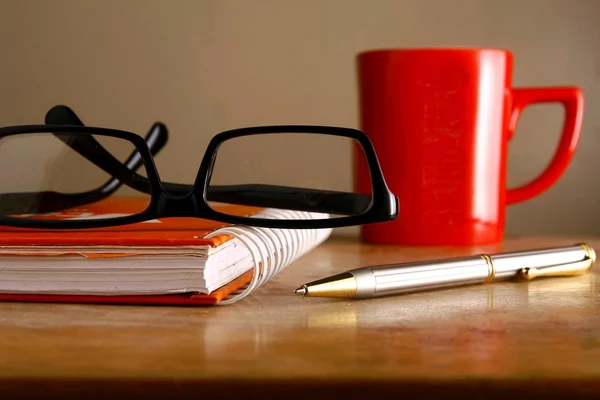 Gafas, taza de café, cuaderno y un bolígrafo — Foto de Stock