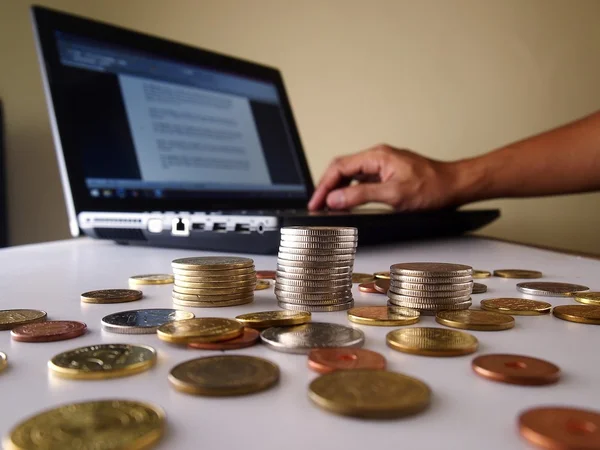 Stapel von Münzen und eine Hand, die an einem Laptop arbeitet — Stockfoto