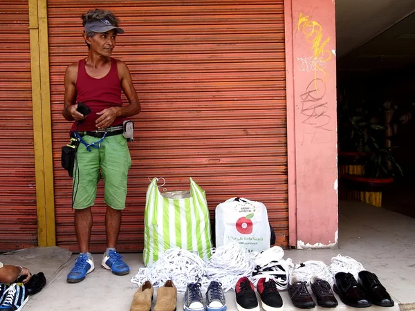 A man sells different kind of shoes at a sidewalk in a street — Stock Photo, Image