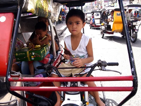 Un niño se sienta en el asiento del conductor de un triciclo —  Fotos de Stock