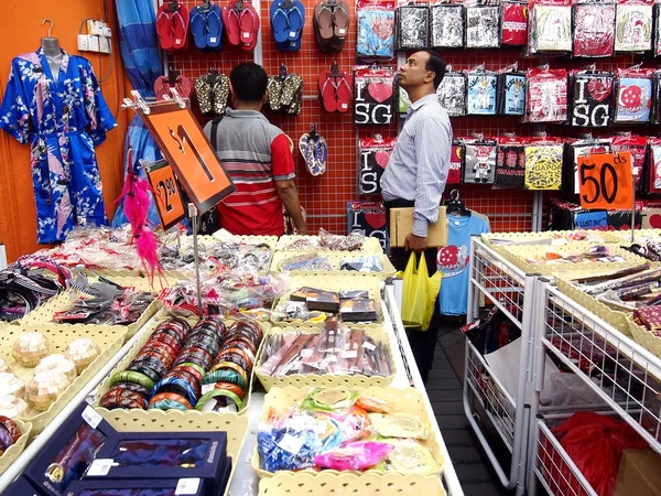 Los turistas eligen entre una variedad de productos de recuerdo en una tienda o tienda en Chinatown, Singapur . — Foto de Stock