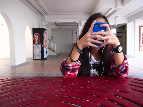 Een jong meisje gebruikt haar mobiele telefoon of smartphone in een studie hall in een Hdb gebouw in Tampines, Singapore — Stockfoto