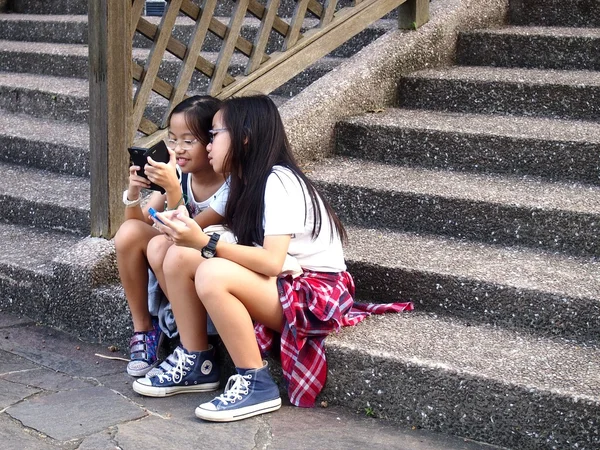 Fiatal lányok használja a mobil vagy smartphone, miközben ül a lépcsőház Tampines, Szingapúr — Stock Fotó