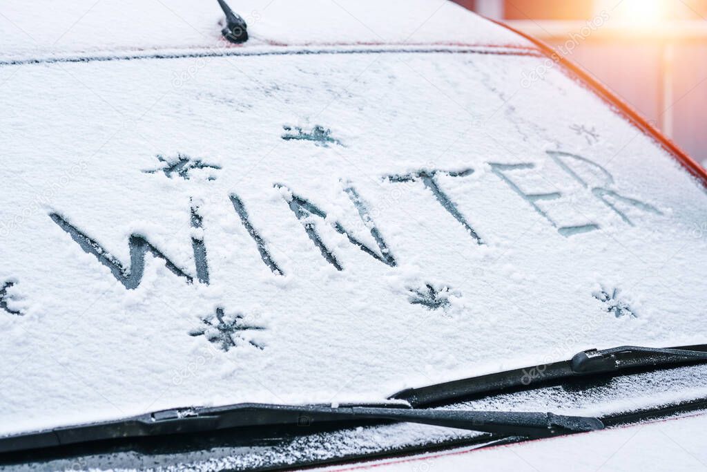word Winter written with finger on a snowy windshield of a car