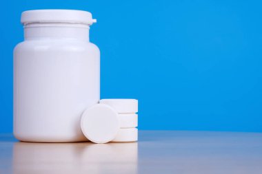 Mavi arka planda büyük beyaz haplar ve ilaç şişesi.. 