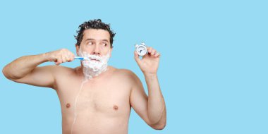 Ağzında diş fırçası olan bir adam, kafasını yıkıyor, tıraş oluyor ve çalar saate bakıyor.