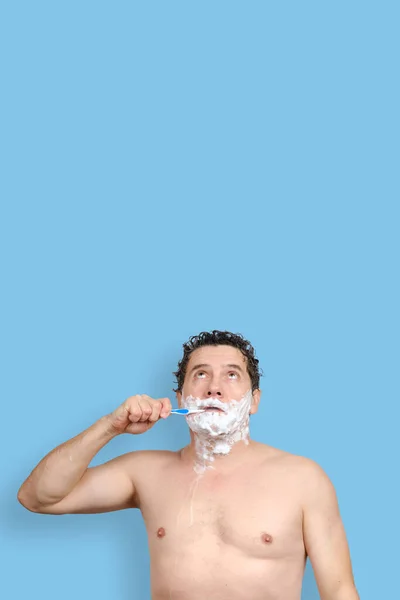 White man holds a toothbrush, shaving and looks up on blue background — Stock Photo, Image