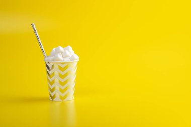 Sarı zemin üzerinde şeker küpleriyle doldurulmuş tek kullanımlık kağıt bardakta saman